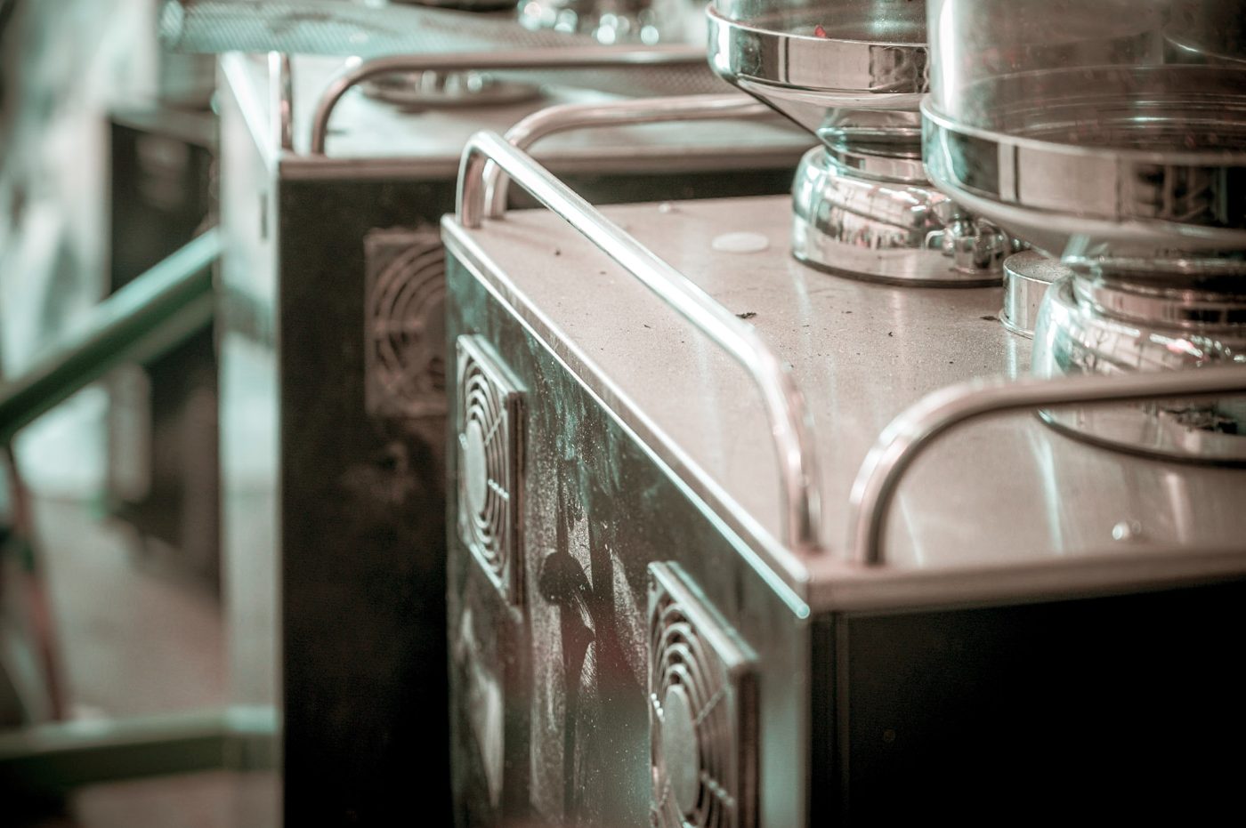 Stainless-steel commercial beverage equipment lined up in a refurbishing bay, showing cooling fans and polished dispenser bowls.